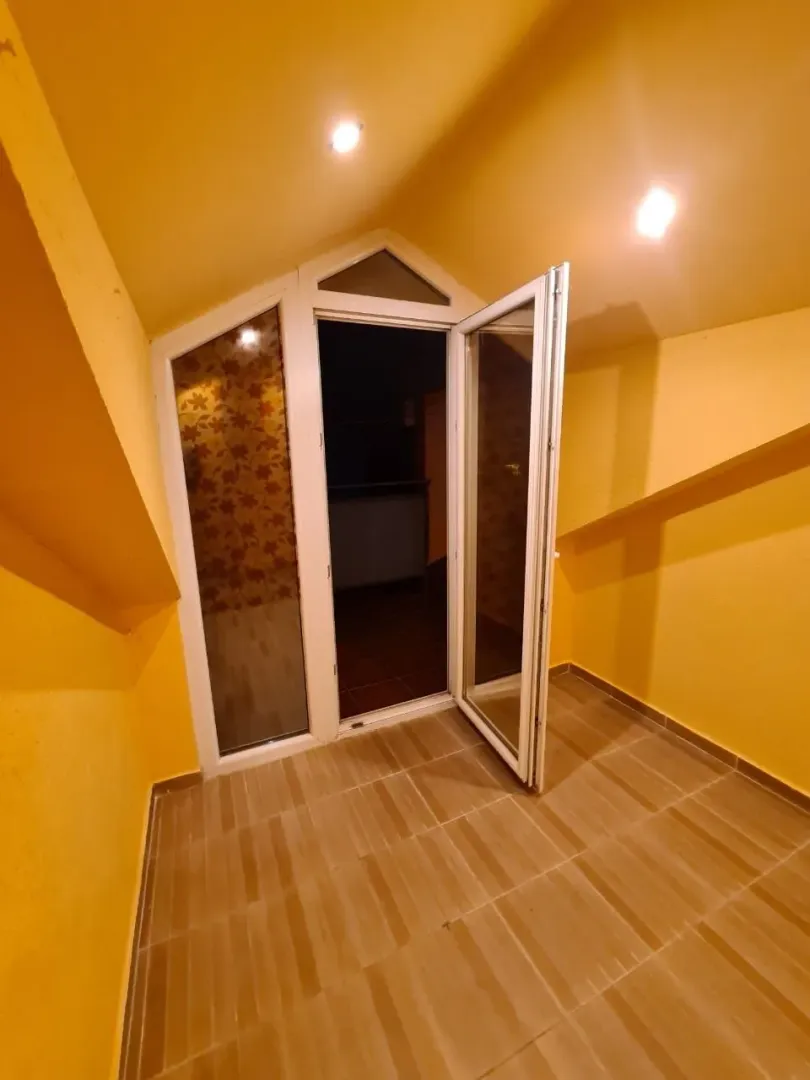 Prazna potkrovna prostorija sa žutim zidovima i izlazom na balkonska vrata.