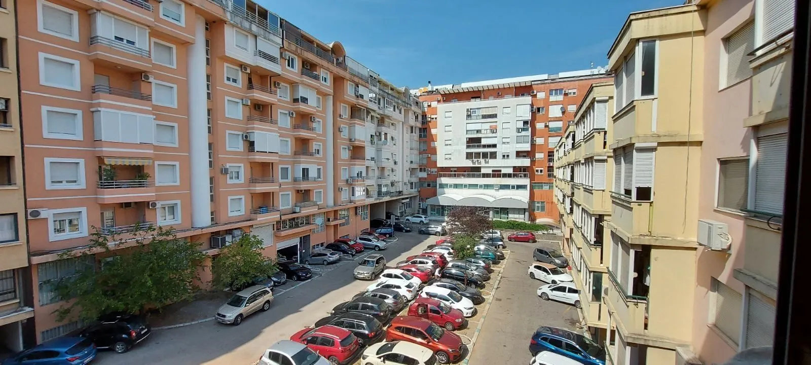 Pogled s prozora na zajednički parking i stambene zgrade.
