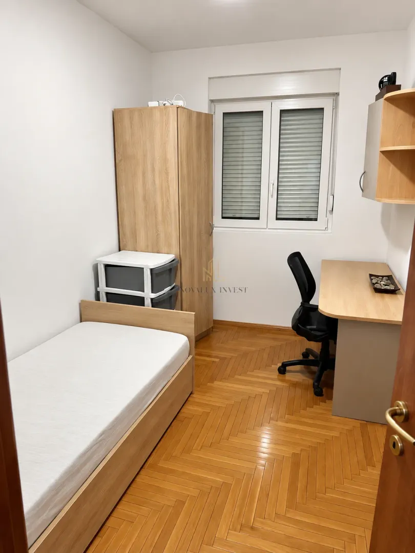 Manja spavaća soba sa krevetom, radnim stolom i ormarom.