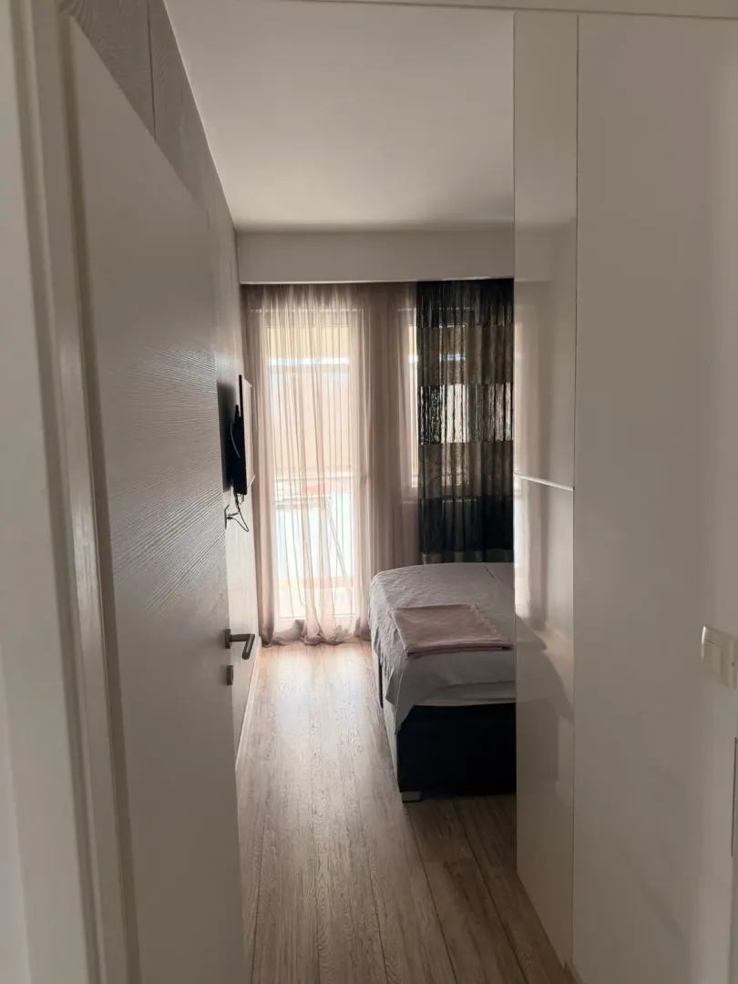 Pogled iz hodnika na spavaću sobu sa krevetom i prozorom.