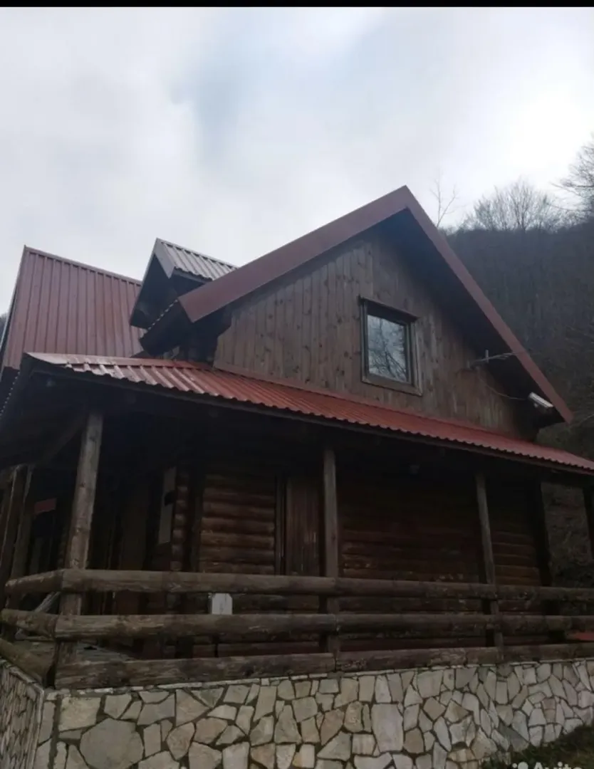 Eksterijer drvene vikendice sa kamenim temeljom i natkrivenom verandom.