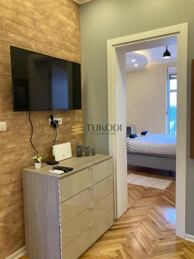 View from the living room towards the bedroom with a bed and parquet flooring.