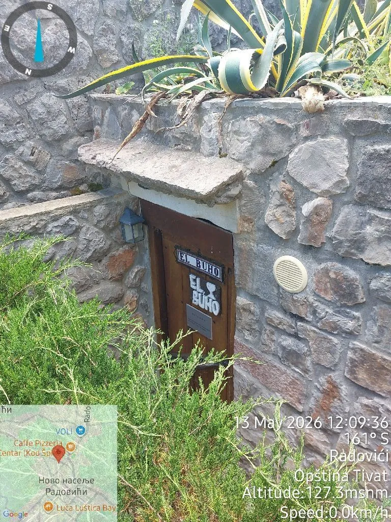 Pogled na kameni ulaz sa drvenim vratima i zelenilom.