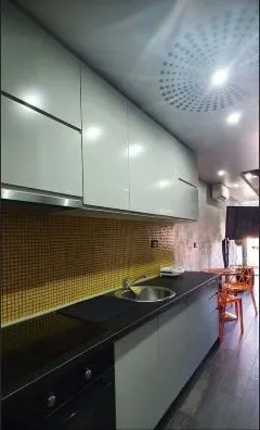 Moderna kuhinja sa bijelim elementima i tamnom radnom površinom.