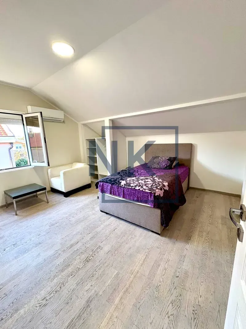 Attic bedroom with a bed, armchair, and open wardrobe.