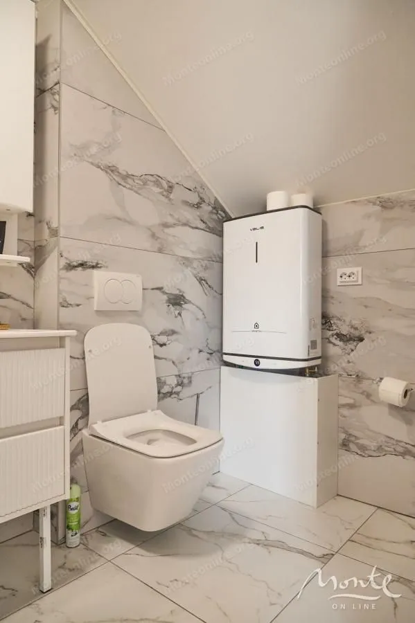 Manje kupatilo sa WC šoljom, umivaonikom i bojlerom pod kosinom.