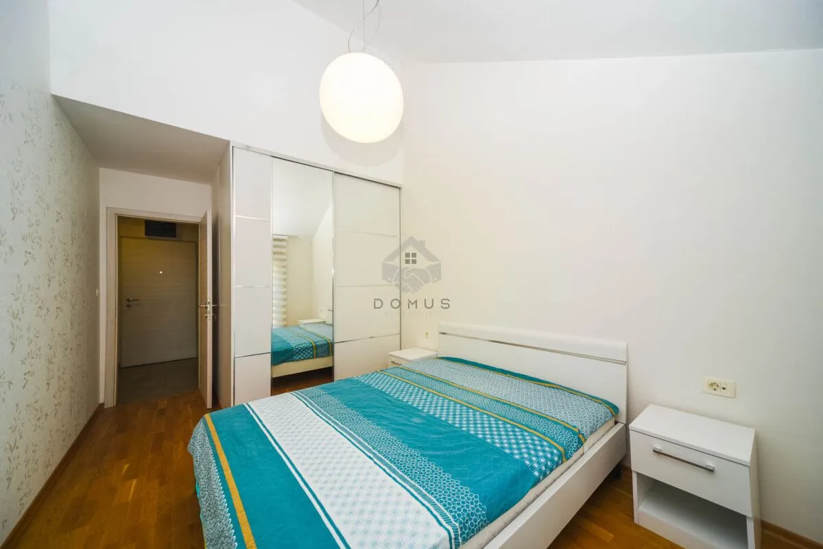 Namještena spavaća soba sa bračnim krevetom, bijelim garderoberom sa ogledalom i noćnim stočićem.