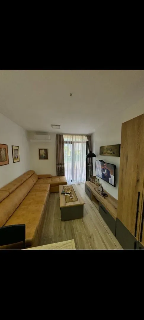 Dnevna soba sa ugaonom garniturom, TV-om i izlazom na terasu.