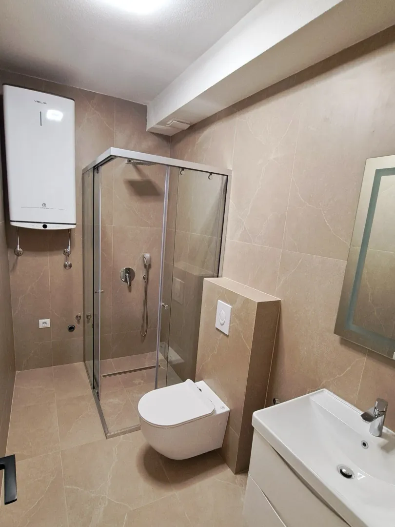 Moderno opremljeno kupatilo sa tuš kabinom, umivaonikom i wc šoljom u bež tonovima.