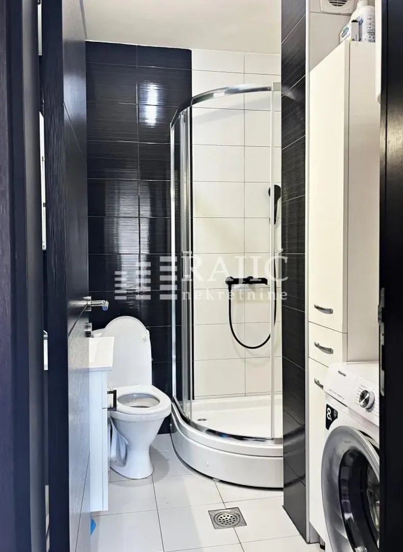 Modern bathroom with a shower cabin, toilet, and washing machine.