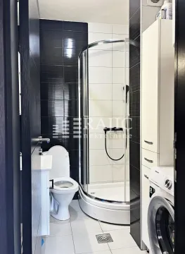 Modern bathroom with a shower cabin, toilet, and washing machine. - image 7