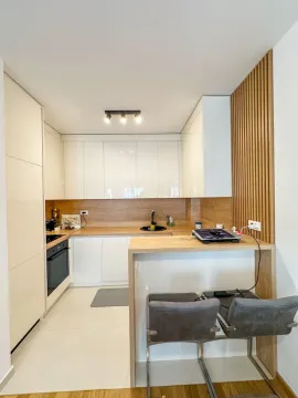 Moderna kuhinja sa bijelim elementima, drvenim detaljima i šankom sa stolicama. - image 3
