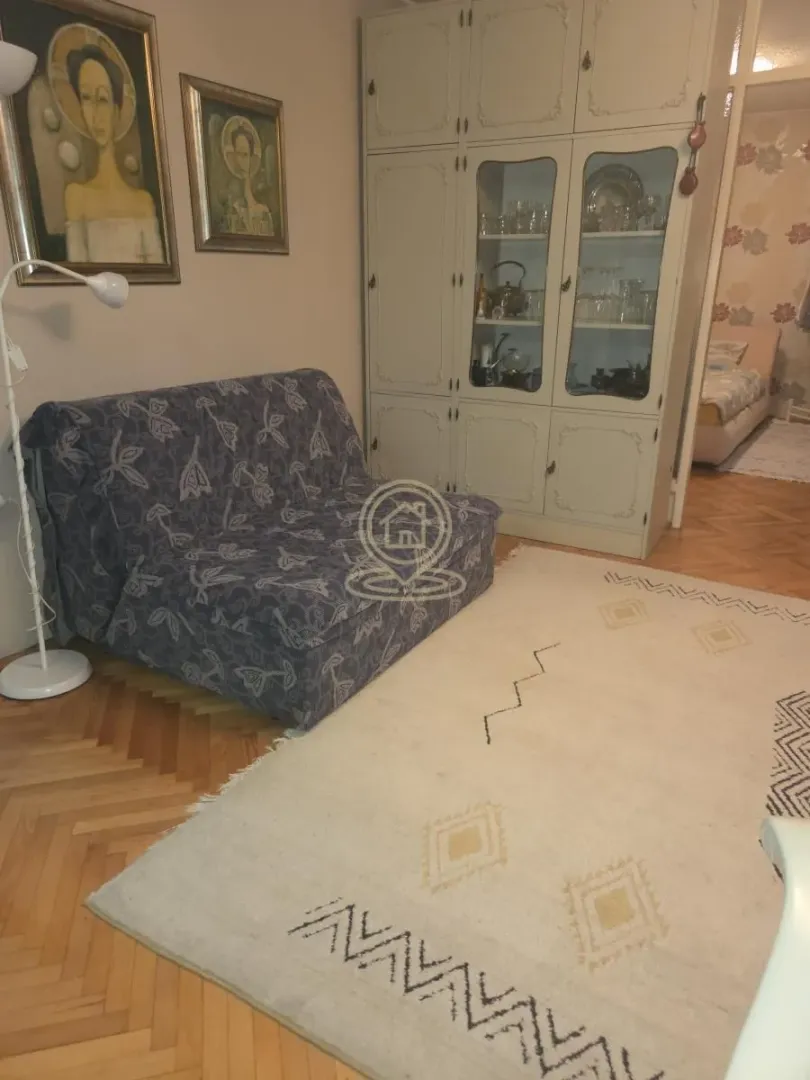 Dnevni boravak sa kaučem, tepihom, vitrinom i slikama na zidu.
