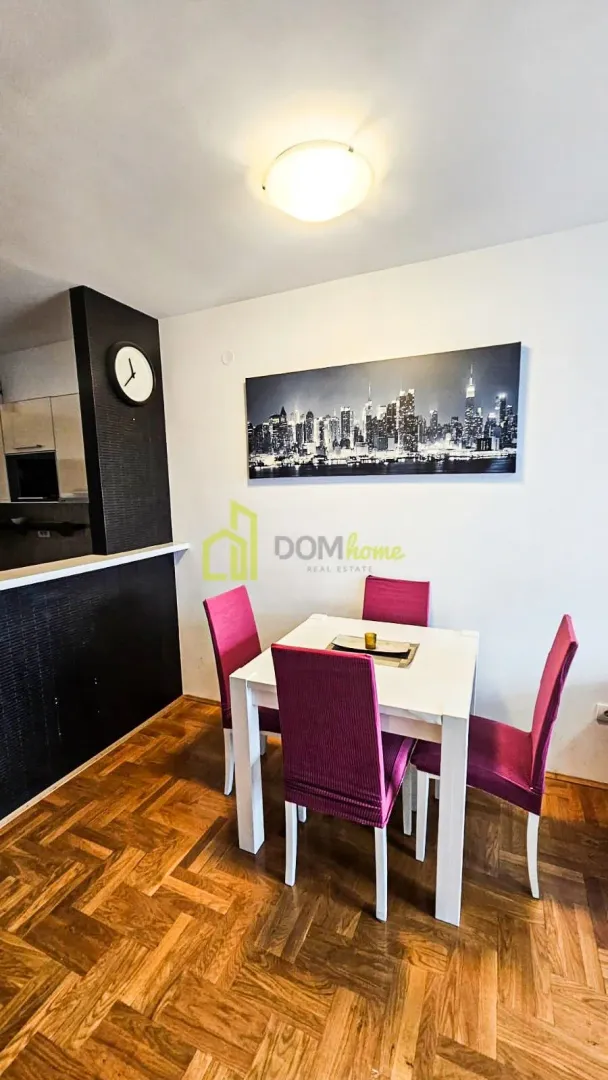 Dining area with a white table and pink chairs against a wall with a cityscape painting.