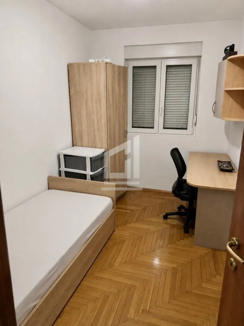 Manja spavaća soba sa krevetom, garderoberom, radnim stolom i parketom na podu.