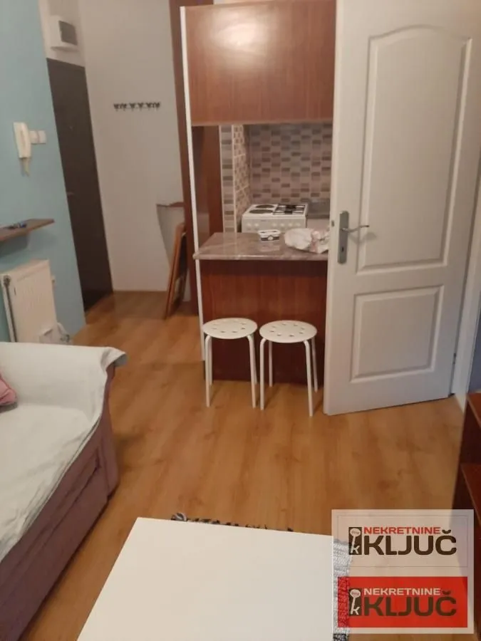Pogled iz dnevne sobe na manju kuhinju sa šankom i stolicama.