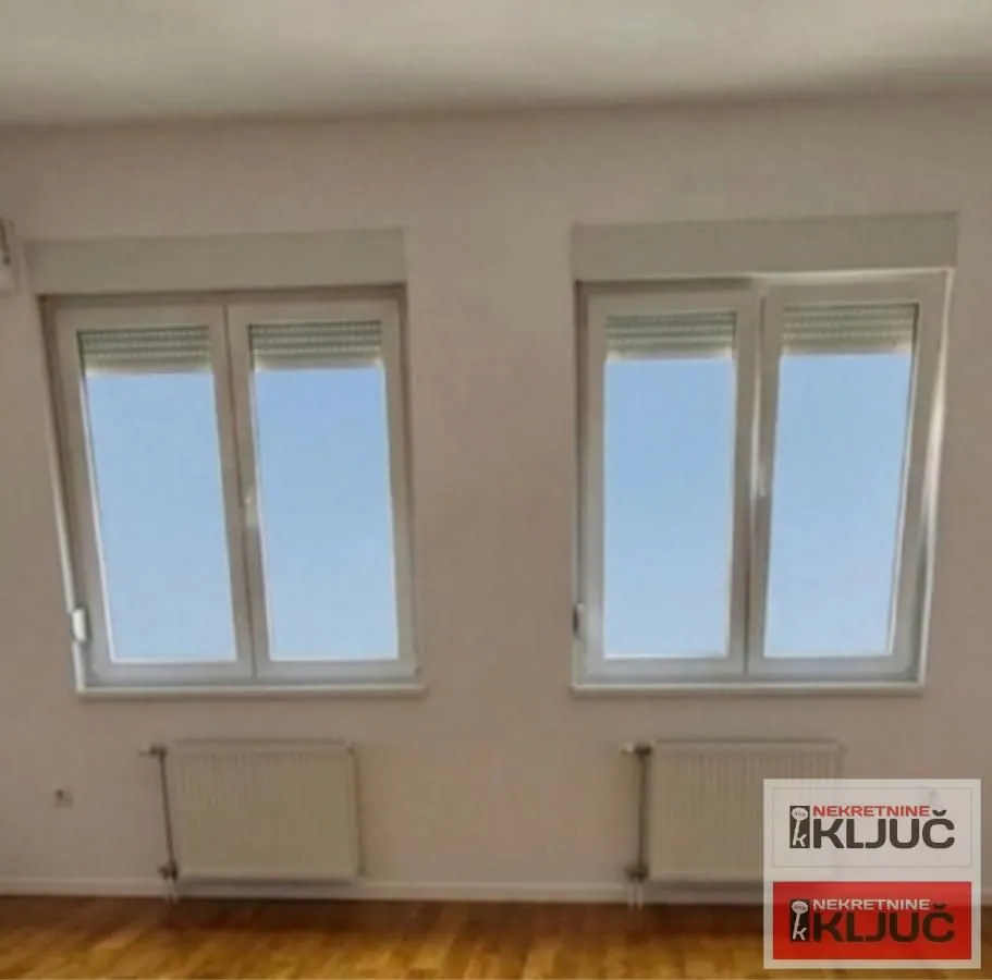 Prazna soba sa dva prozora i radijatorima.