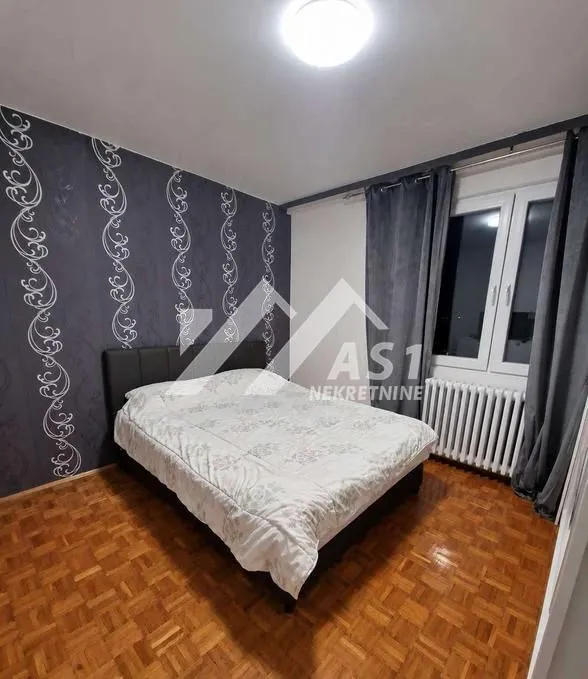 Spavaća soba sa bračnim krevetom, parketom i tapetom na zidu.