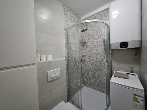 Modern bathroom with a shower cabin, water heater, and washing machine. - image 3