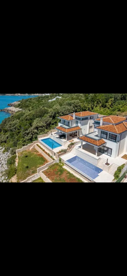 Pogled iz vazduha na moderne vile sa bazenima blizu obale mora.