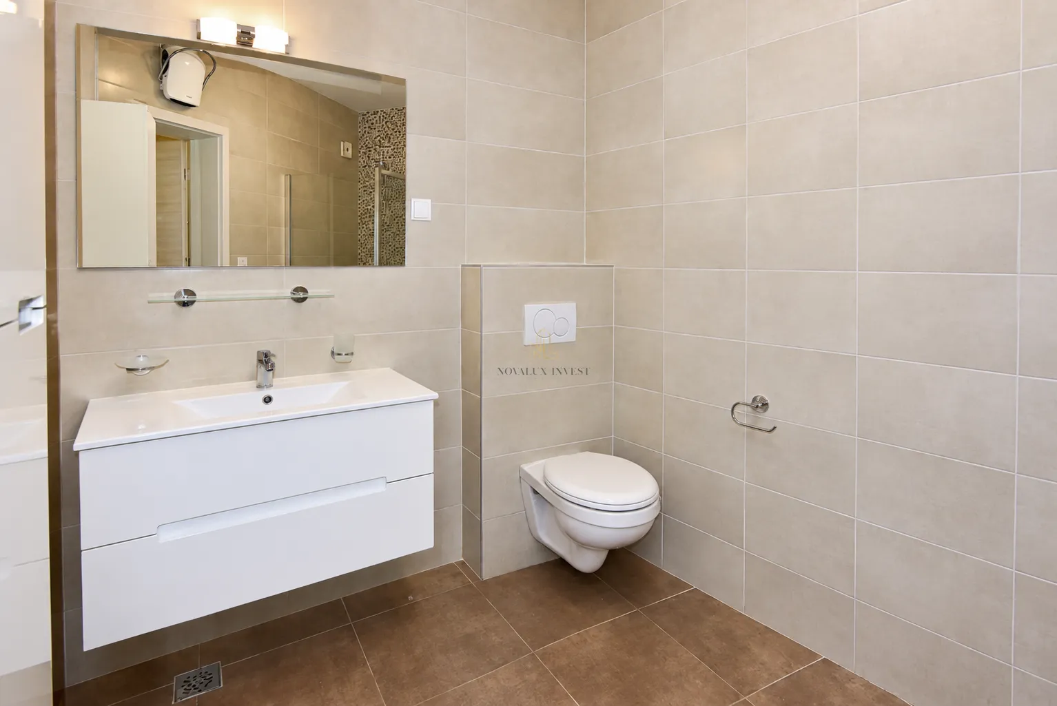 Moderne kupatilo sa umivaonikom, ogledalom i konzolnom wc šoljom obloženo pločicama u neutralnim tonovima.
