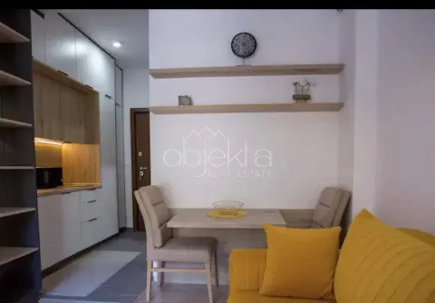 Living room with a sofa, dining table, and kitchen in the background. - image 5