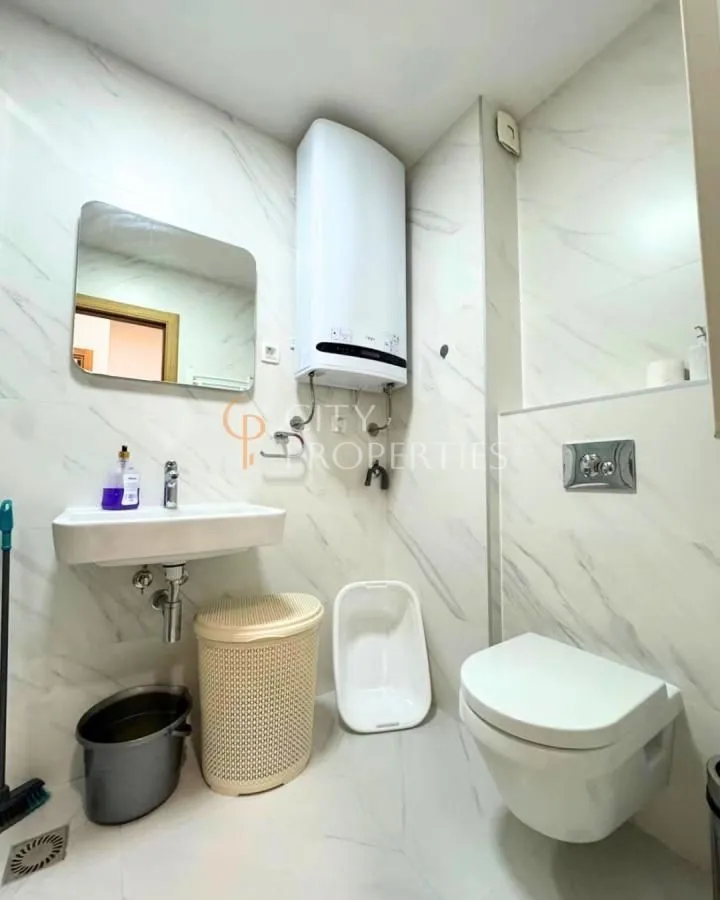 Manje kupatilo sa tuš kabinom, umivaonikom i wc šoljom obloženo svijetlim pločicama.