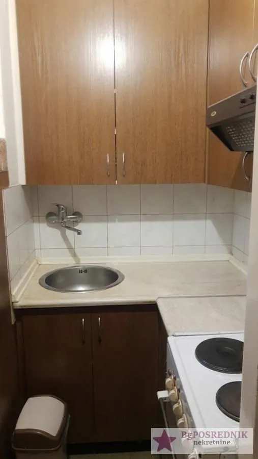 Manja kuhinja sa sudoperom, drvenim elementima i šporetom.
