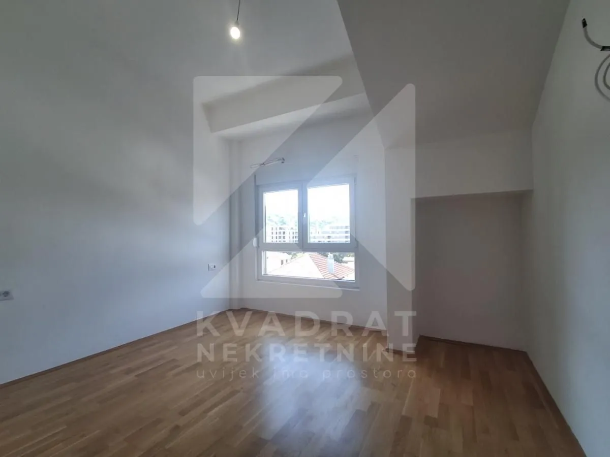 Empty room with hardwood flooring and a single window.