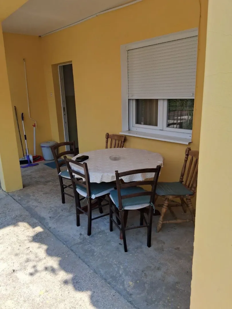 Covered terrace with a table and chairs in front of the house entrance.