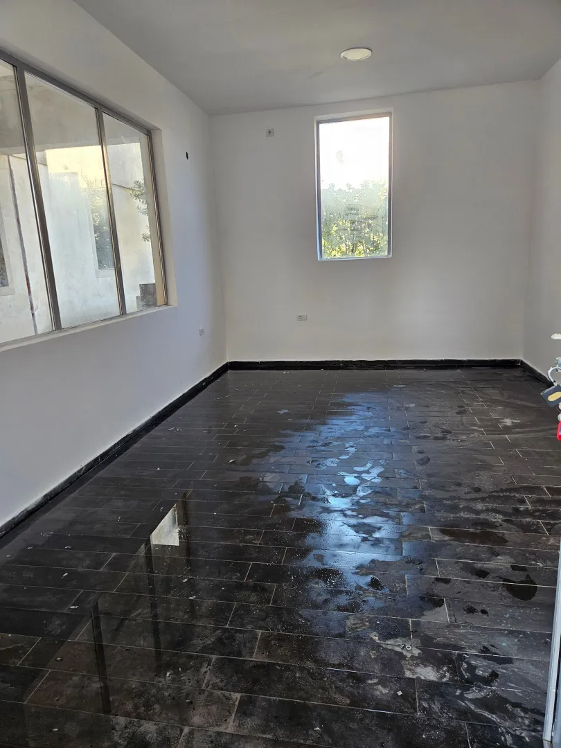 Empty room with dark ceramic floor tiles and large windows.