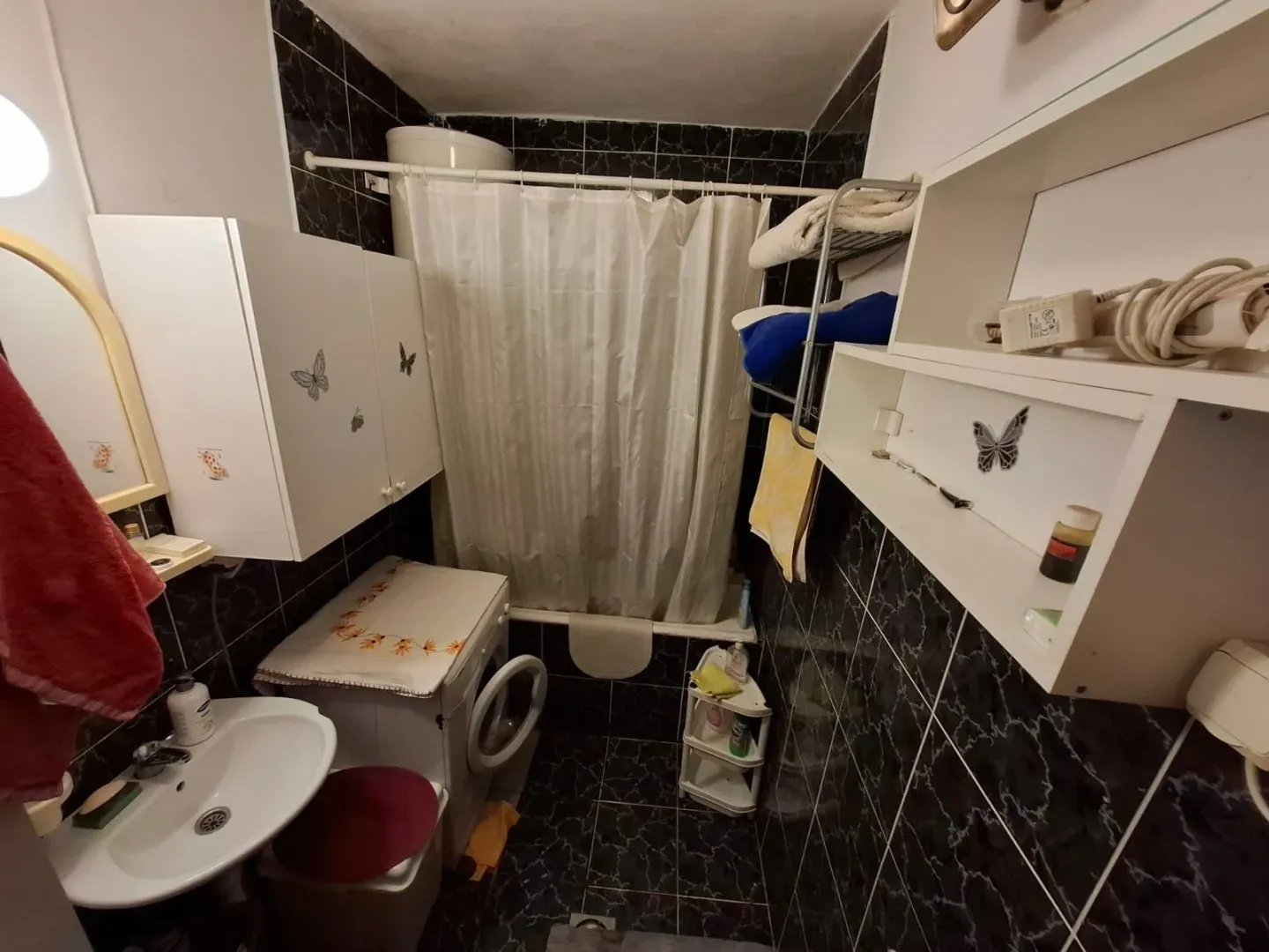 Kompaktno kupatilo sa kadom, umivaonikom, veš mašinom i bijelim zidnim elementima.