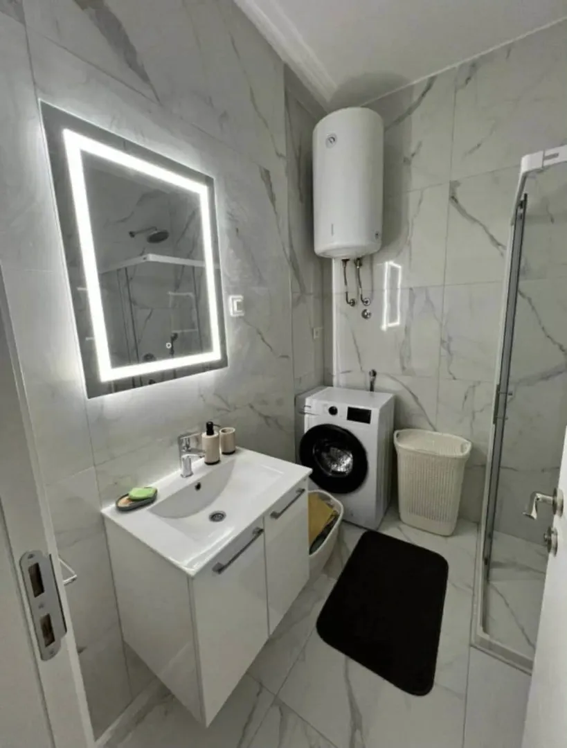 Modernly equipped bathroom with light marble tiles, a vanity, and a walk-in shower.