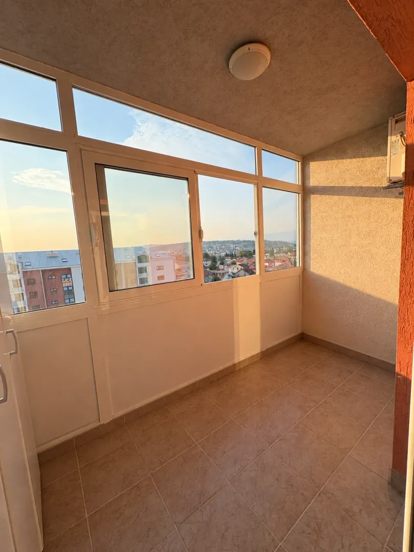 Zastakljeni balkon sa pločicama na podu i pogledom na grad.