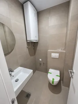 Manje kupatilo obloženo bež pločicama sa ugradnim toaletom, umivaonikom i bojlerom. - image 8