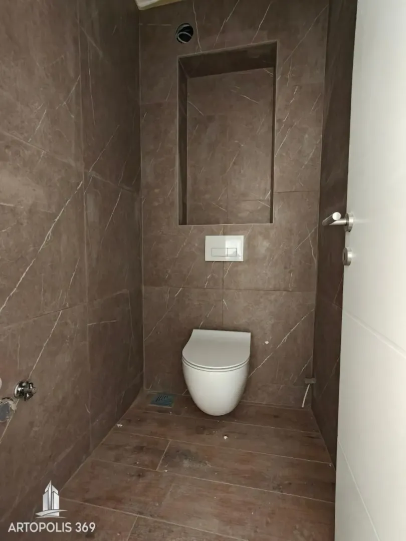 Manje kupatilo obloženo keramičkim pločicama u braon tonovima sa ugradnom šoljom.