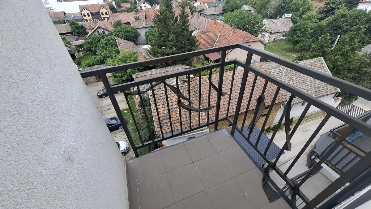 Manji popločani balkon sa crnom metalnom ogradom i pogledom na naselje.