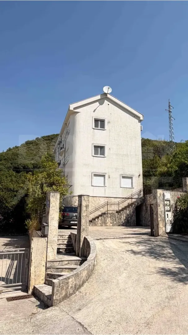 Pogled na spoljašnjost višestambene zgrade sa dvorišnim ulazom i parkingom.