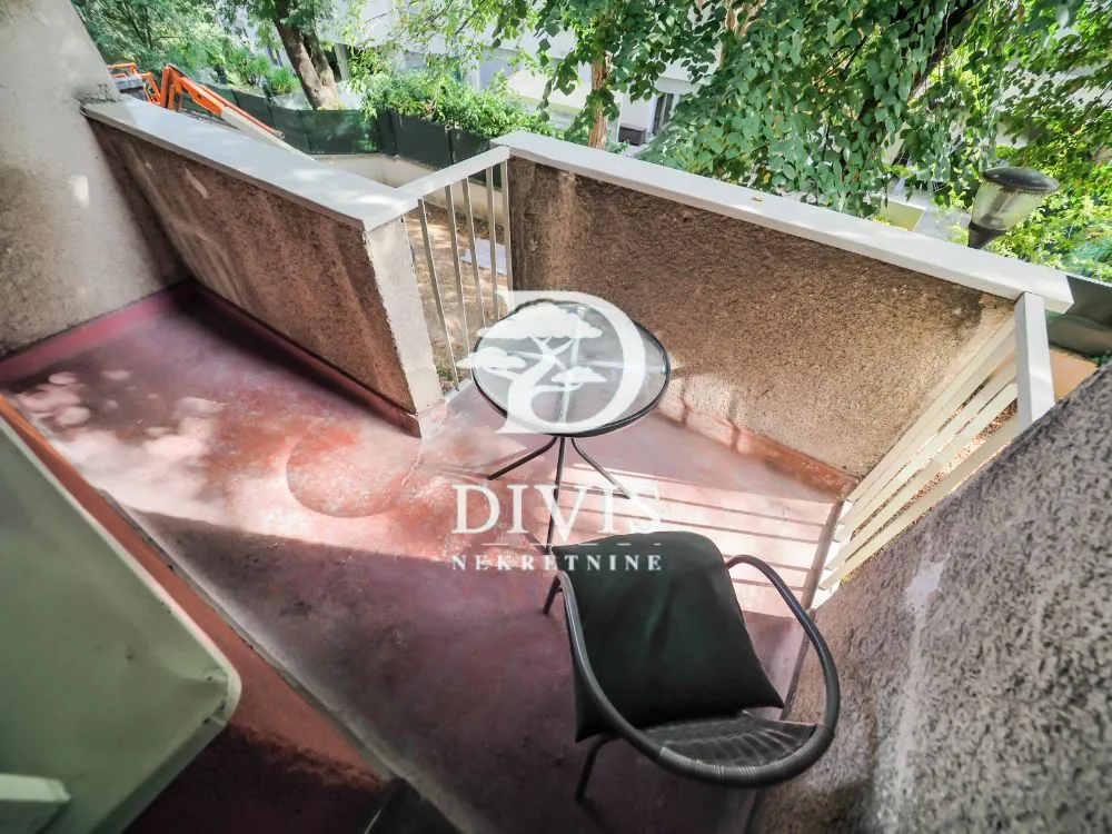 Small balcony with a table and chair and a view of greenery.