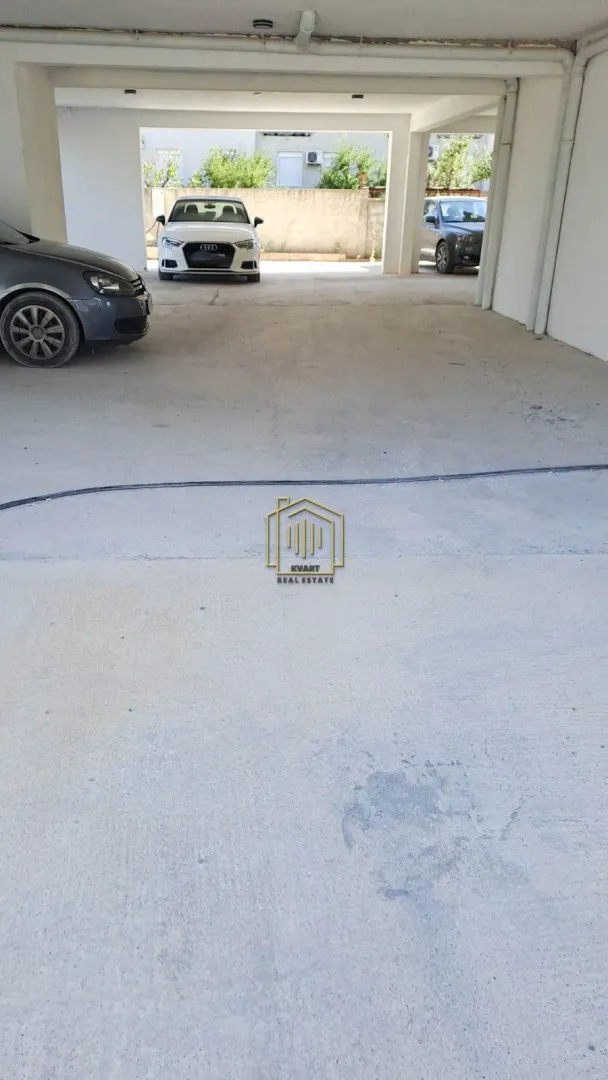 Natkriveni parking prostor u prizemlju zgrade sa parkiranim automobilima.