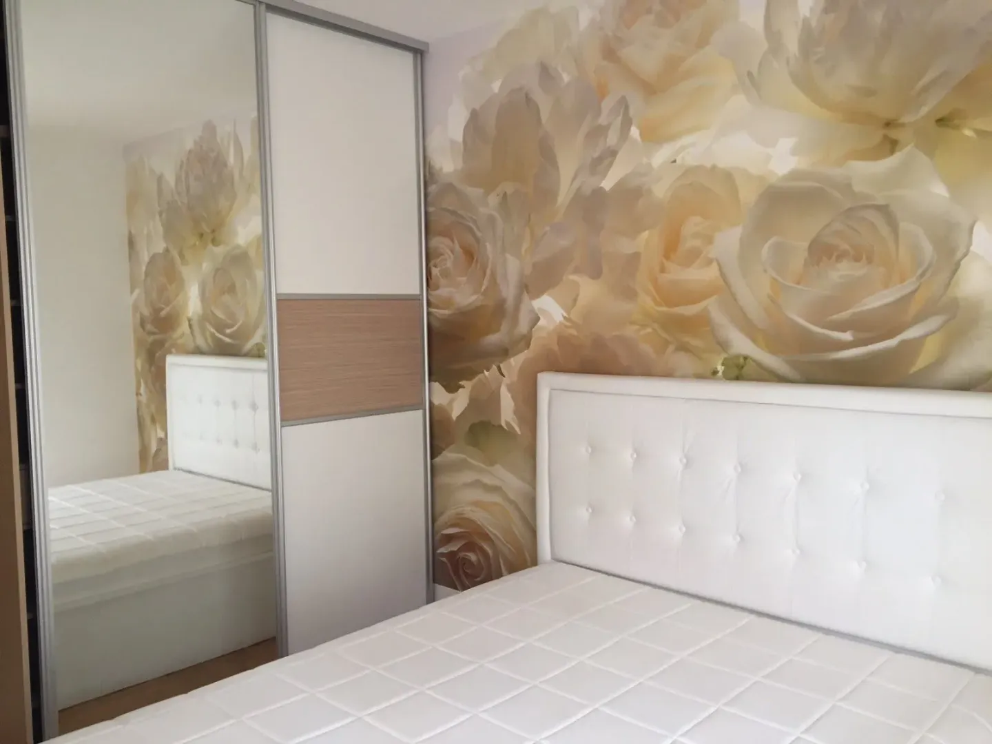 Bedroom with a white bed, mirrored wardrobe, and rose-patterned wallpaper.