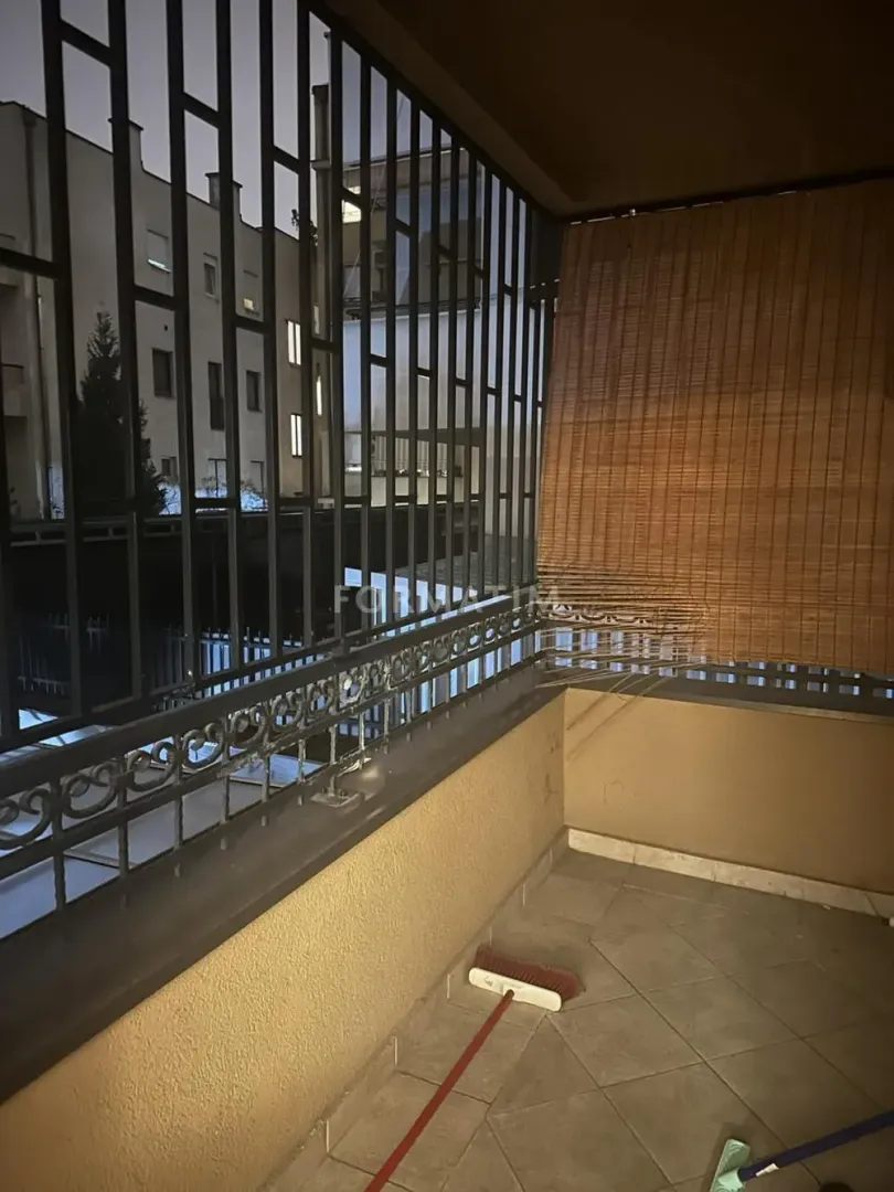 Covered balcony with a metal railing and roller blind at night.