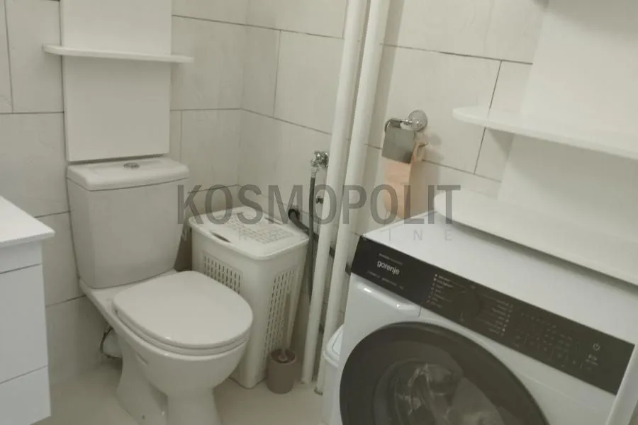Kupatilo opremljeno toaletom, veš mašinom i policama.