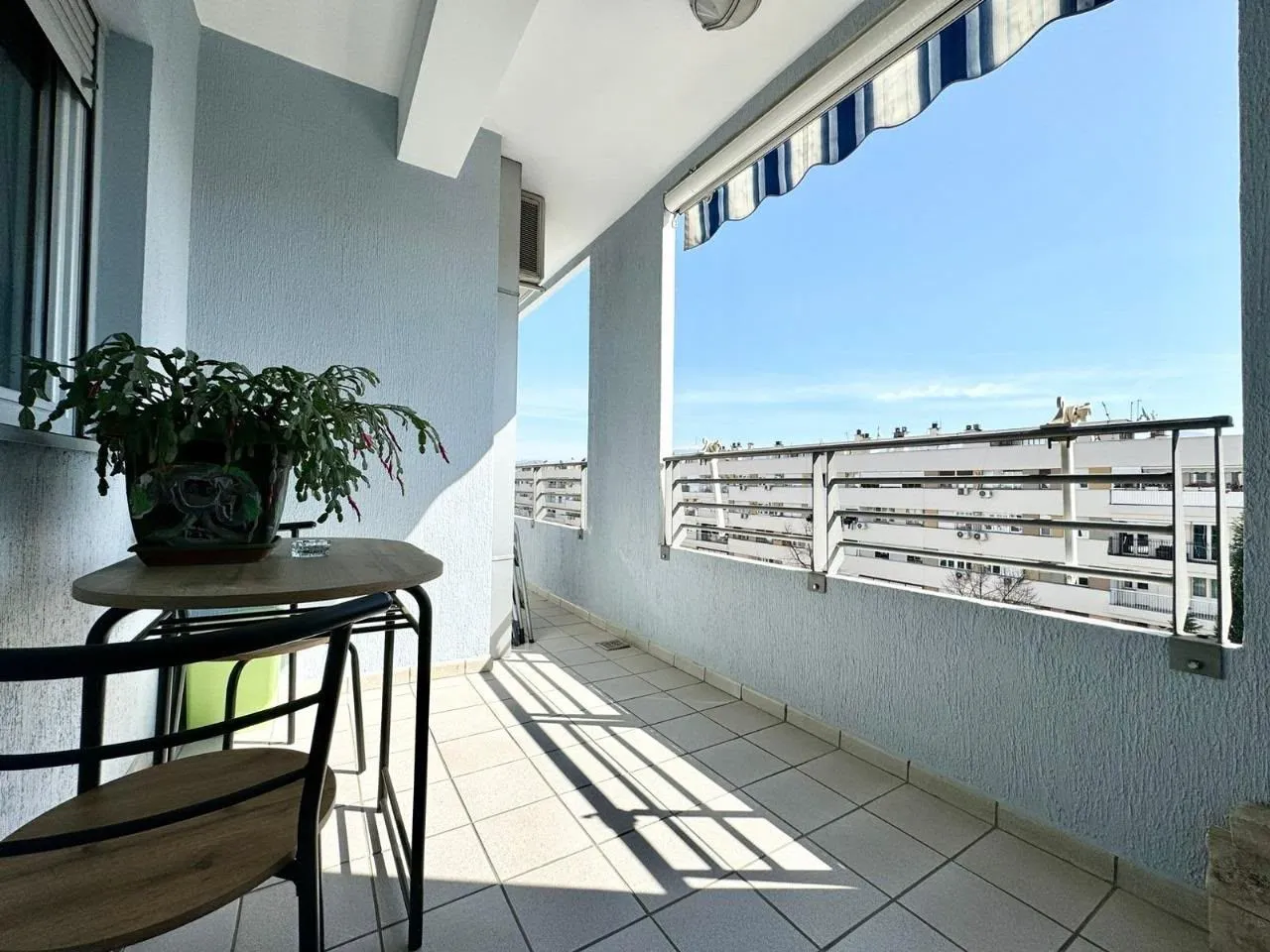 Bright balcony with a table, chairs, and awning.
