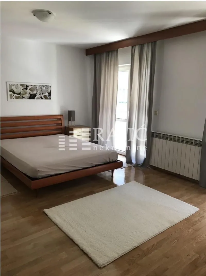 Prostrana spavaća soba sa bračnim krevetom, drvenim parketom i izlazom na terasu.