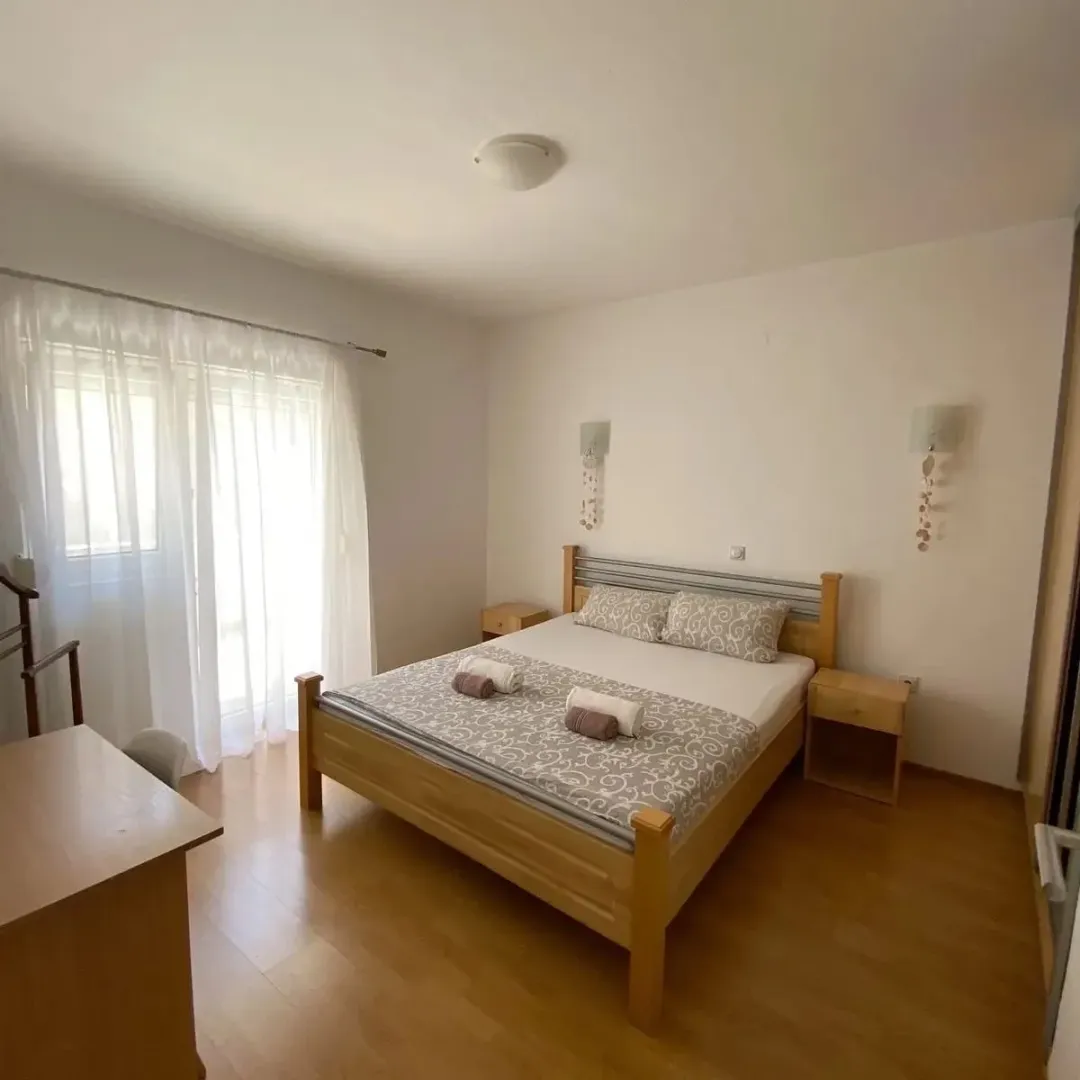 Spavaća soba sa bračnim krevetom, noćnim stočićima i prozorom sa zavjesama.