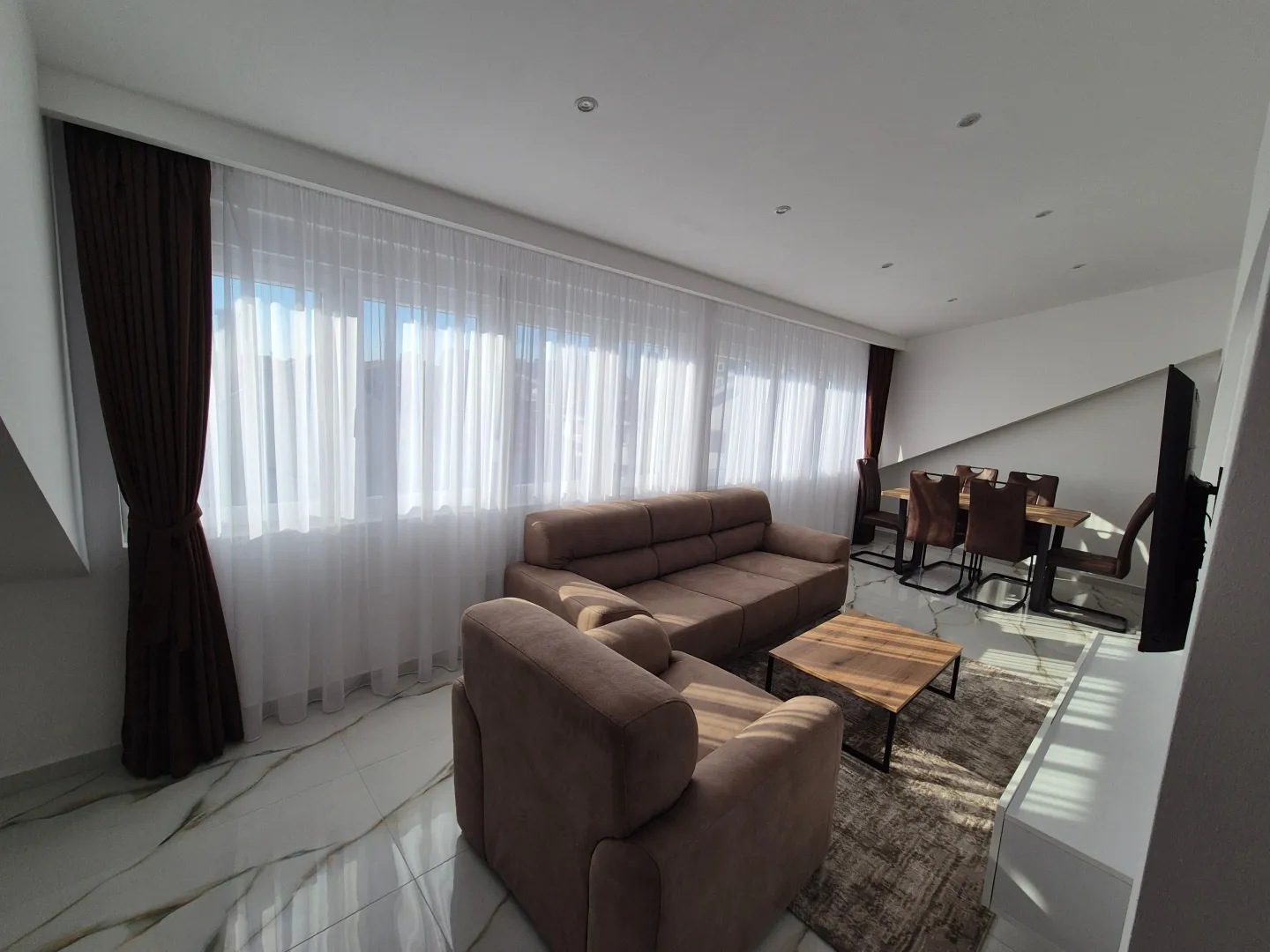 Living room with sofa, coffee table, and dining area next to a large window.