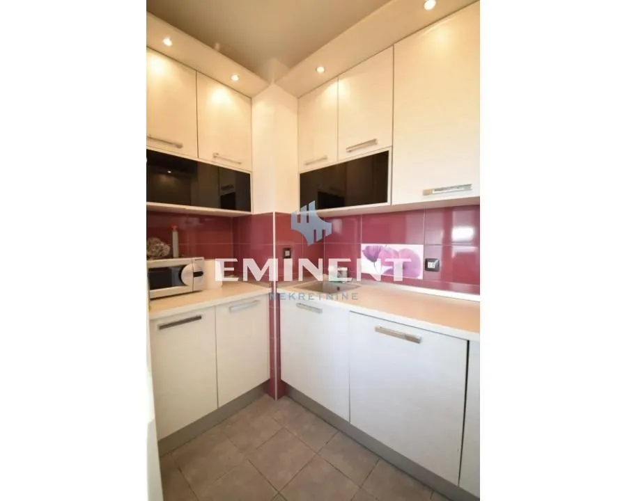 Small kitchen with white units and red wall tiles.