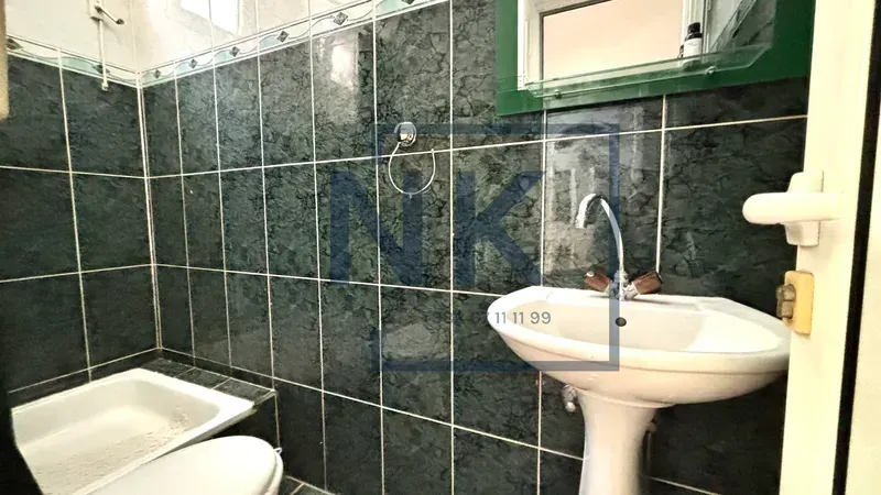 Kupatilo obloženo tamnim pločicama sa umivaonikom i wc šoljom.