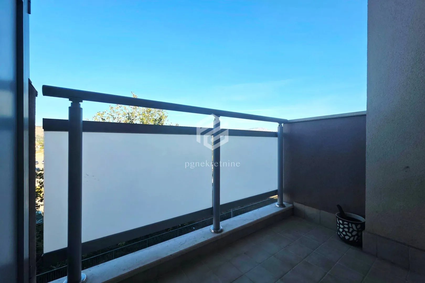 Manji natkriveni balkon sa popločanim podom i metalnom ogradom.